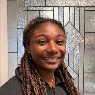 Patient Care Coordinator Janiah Smiling In Front Of Glass Door